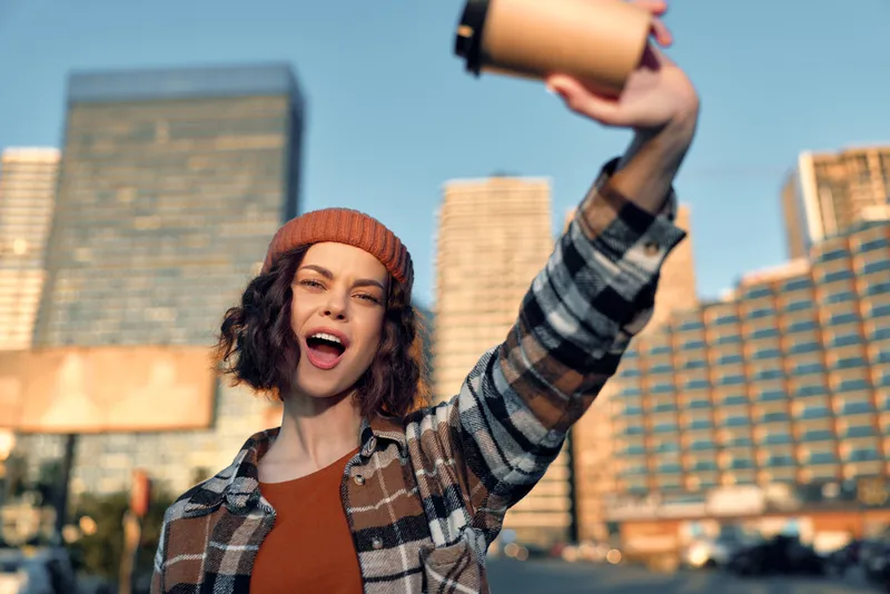 Woman coffee city smile beanie plaid candid golden moment at golden hour glow, authenticity and mindful living captured in an emotional storytelling urban candid lifestyle portrait.