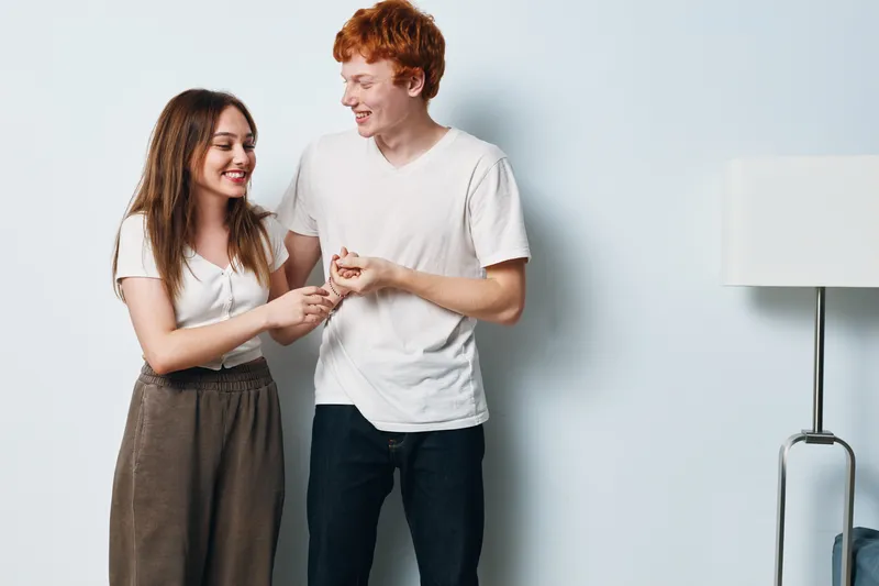 Young couple standing and smiling together in cozy home interior with modern white wall and floor lamp for lifestyle and happy relationship moments.