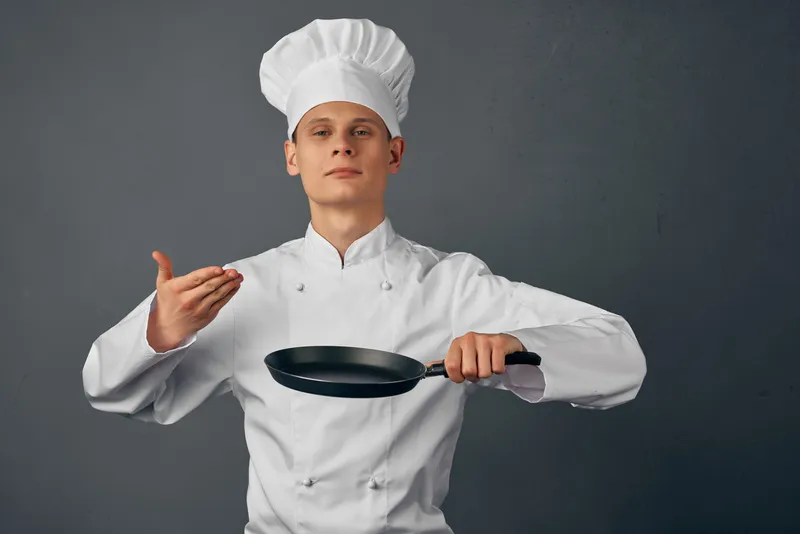 Весёлый повар в униформе держит сковороду в руках и готовит в ресторане