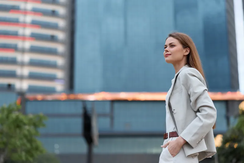 Confident woman in business attire standing outdoors with a modern urban backdrop, exuding professionalism and ambition in a contemporary cityscape.