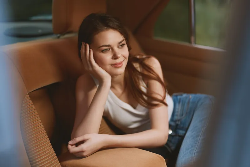 Young woman relaxing in a vintage car, wearing a casual white tank top and jeans, conveying a sense of tranquility and nostalgia.