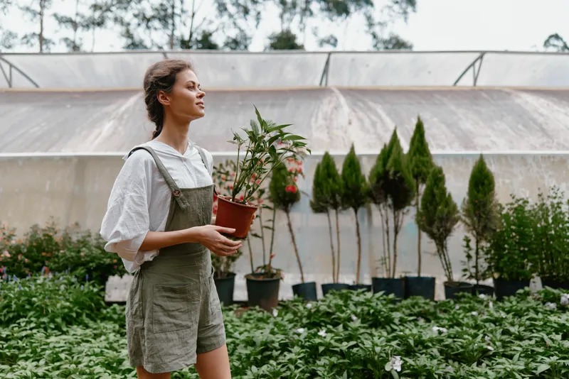 Young woman in casual clothing caring for plants in a greenhouse, showcasing love for nature and gardening, highlighting emotions of serenity and connection to nature