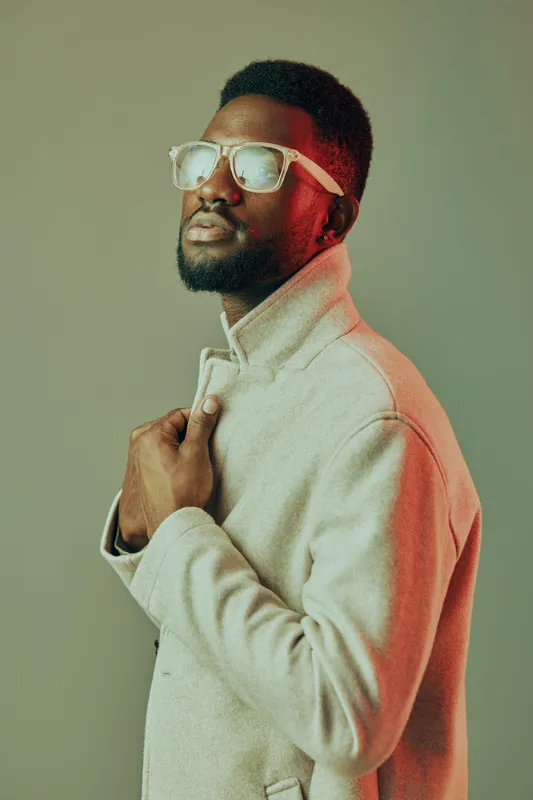 Fashionable young man in stylish coat and sunglasses, showcasing confidence and modern style against a gradient background, perfect for seasonal fashion inspiration