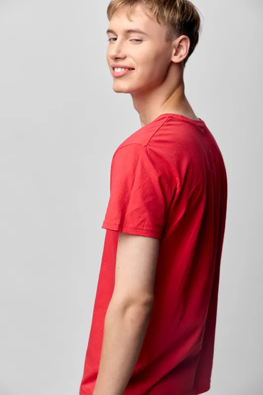 Young man in red tee smiles over the shoulder in a casual fashion setup, bright studio lighting highlights a relaxed mood suitable for lifestyle, fashion, and everyday wear projects