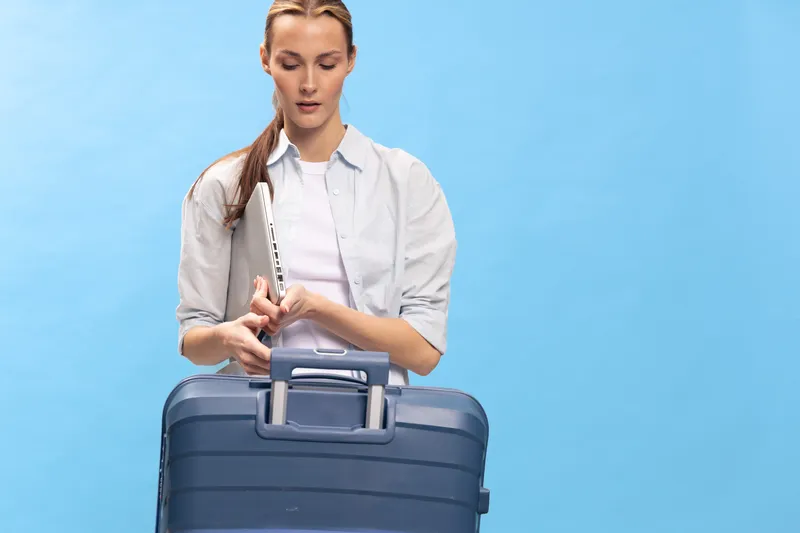 Young woman in casual clothes stands with blue suitcase and holds white flute on blue background. Concept for travel, music, and leisure lifestyle with musical instrument and luggage.