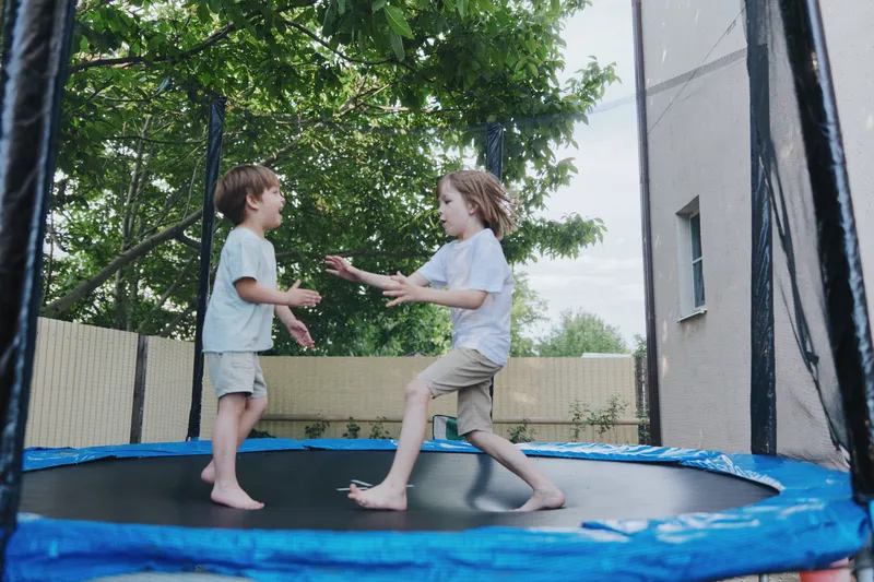 Happy children playing on a trampoline, enjoying a sunny day outdoors in a vibrant green setting. Their laughter fills the air as they leap joyfully.