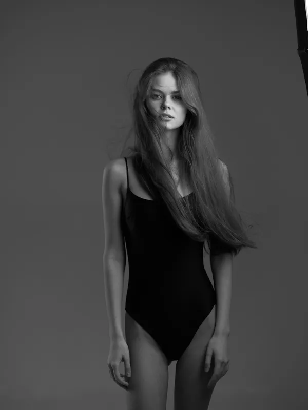 black and white portrait of a young woman in a black swimsuit with long hair and serious expression