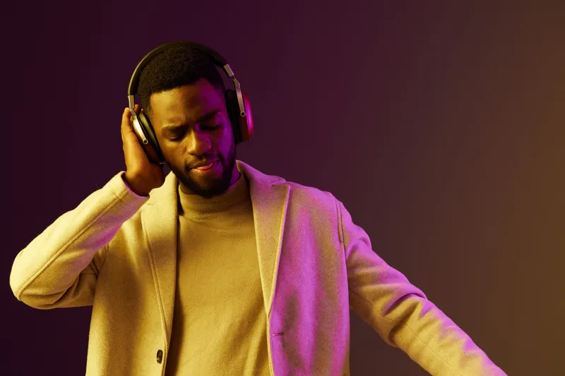 Stylish Black man enjoying music with headphones in a vibrant, purple background, expressing happiness and relaxation, perfect for lifestyle and music themes