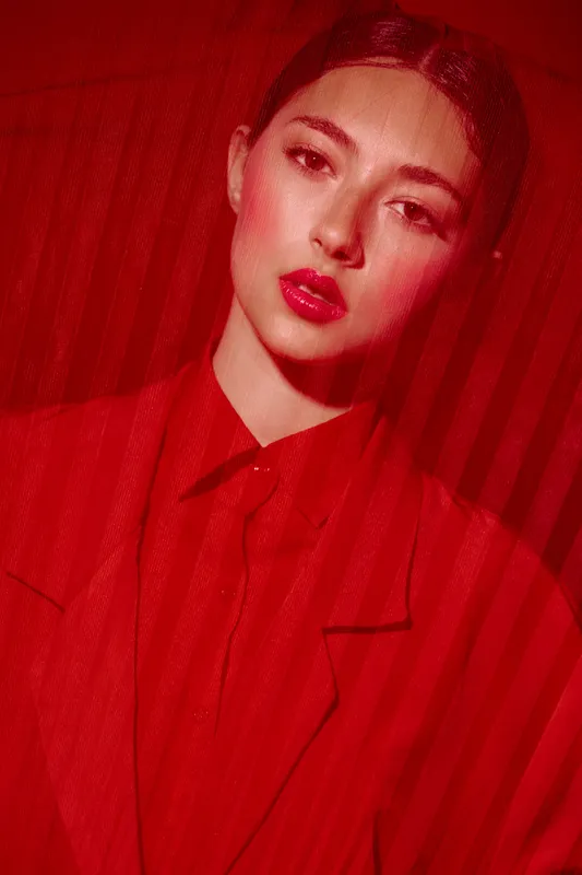 Portrait of a young woman with makeup and lipstick behind a sheer red fabric. Creative beauty theme with red fashion styling and dramatic lighting for editorial concept.