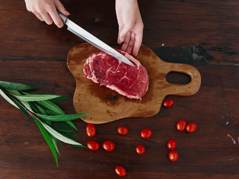 Женщина с ножом в руке нарезает свежее мясо для стейка, предназначенное для запекания на кухне
