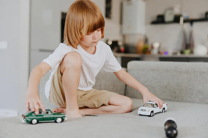Young boy playing with toy cars in a modern living room, showcasing creativity and imagination in a cozy environment.