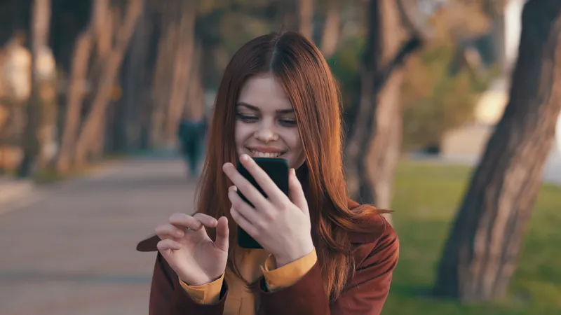 Симпатичная женщина в пальто с телефоном в руке гуляет в парке, отдых