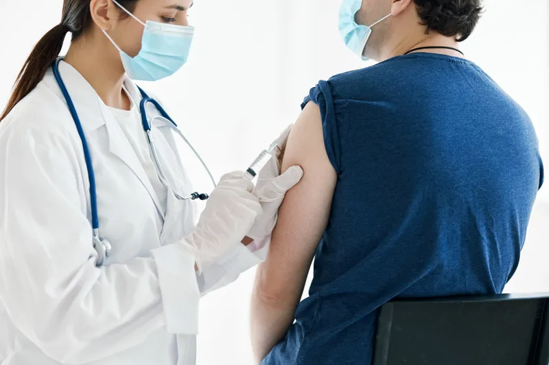 Медсестра в медицинской маске делает инъекцию вакцины в плечо пациента-мужчины