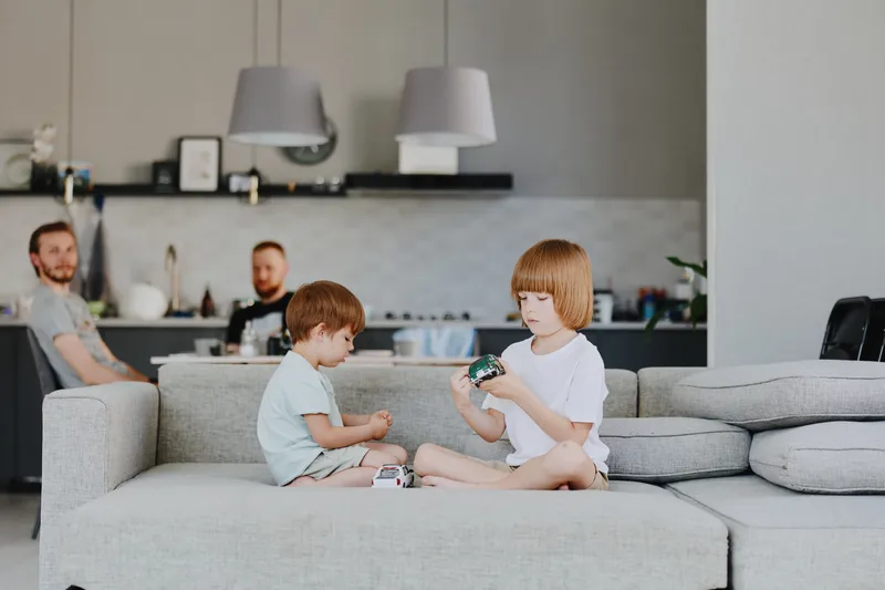 Happy children playing together on the couch, enjoying a playful moment in a cozy living room setting with family members nearby.
