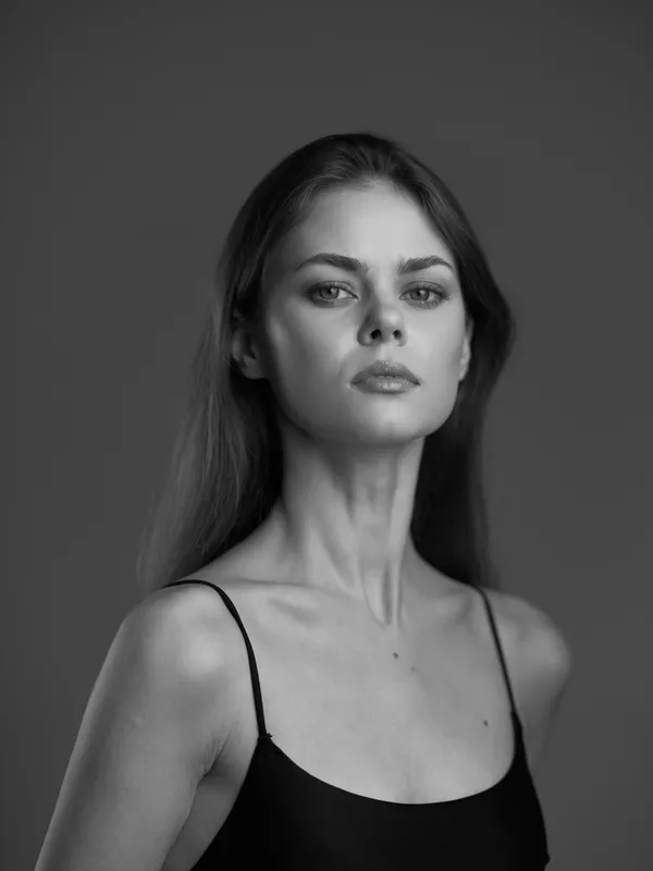 Portrait of a serious woman in black and white wearing a black top with thin straps, showcasing elegance and confidence.