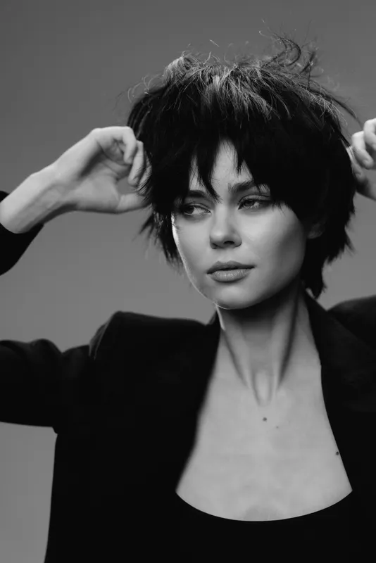 Black and white portrait of a confident woman with short hair expressing calmness and style in a minimalist setting.