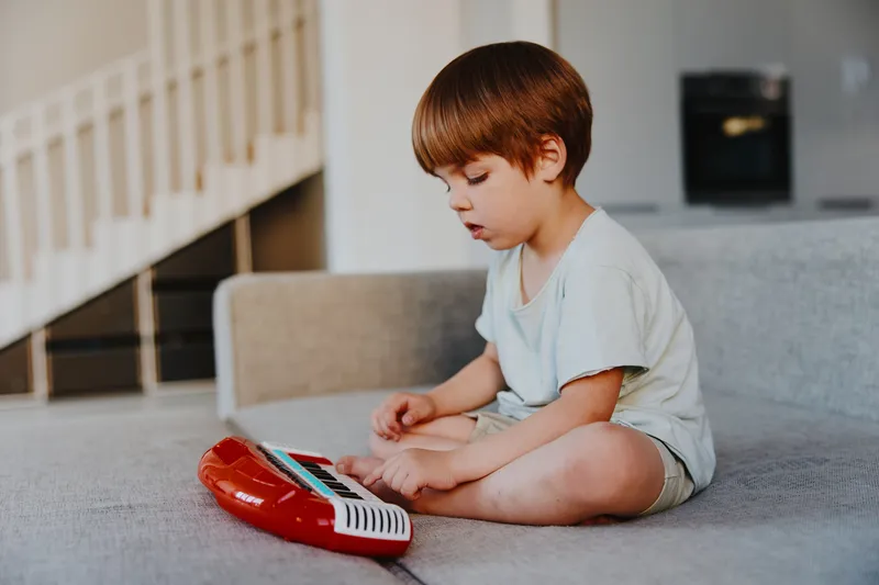 Curious boy playing with a colorful keyboard, exploring music and creativity in a cozy indoor setting, dressed casually in light clothing.