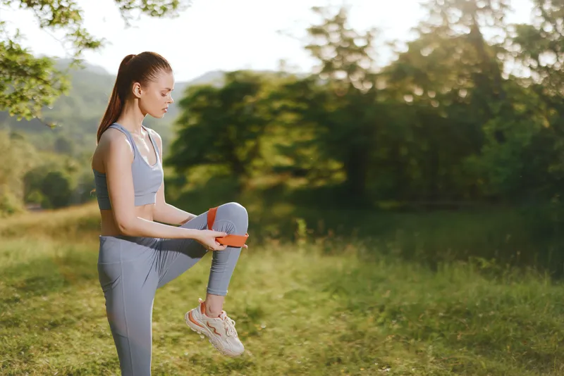 Young woman in blue activewear practicing outdoor leg exercises in a green park, showcasing fitness, strength, and healthy lifestyle