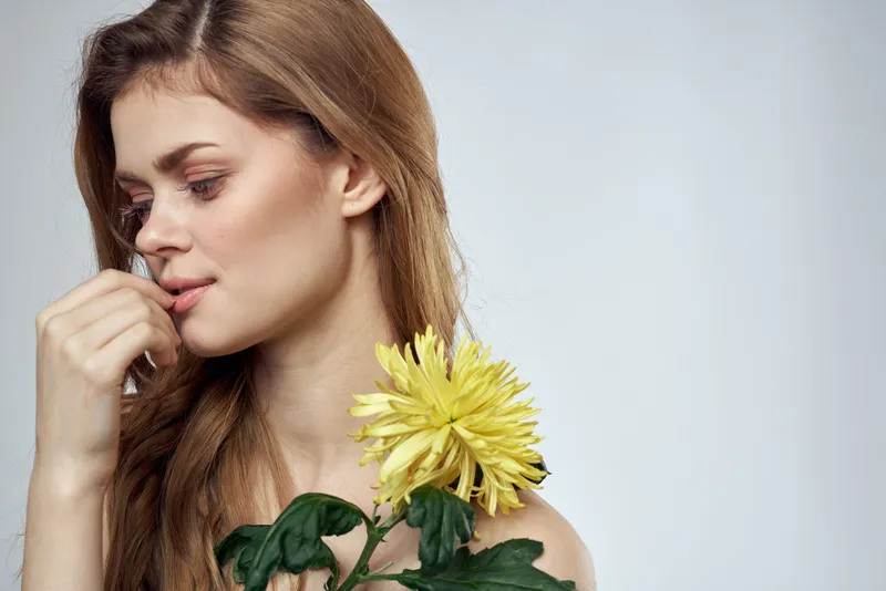 Молодая женщина с желтой хризантемой у лица на сером фоне