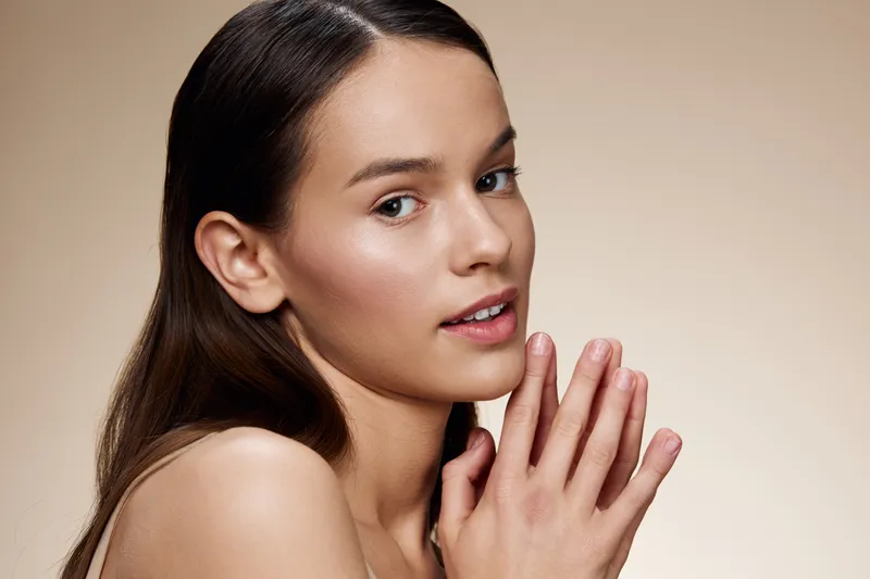 Close up portrait of a young woman with a serene expression, showcasing healthy skin and natural beauty against a neutral background, emphasizing authenticity and elegance