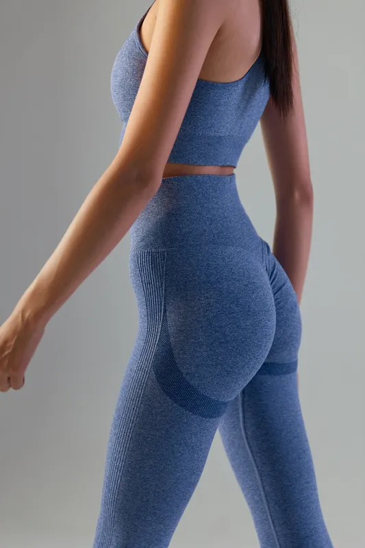 Sport fitness woman wearing stylish blue seamless workout leggings and crop top, posing in minimalistic gray studio background for active lifestyle and body training.
