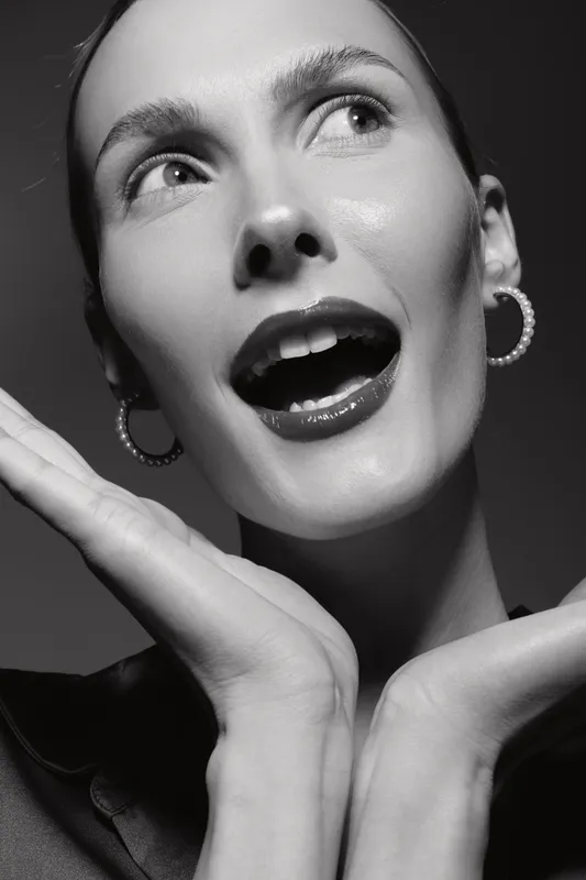 Portrait of a white woman with light skin posing surprised, hands near face. Black and white studio shot with dramatic lighting, fashion and beauty concept.
