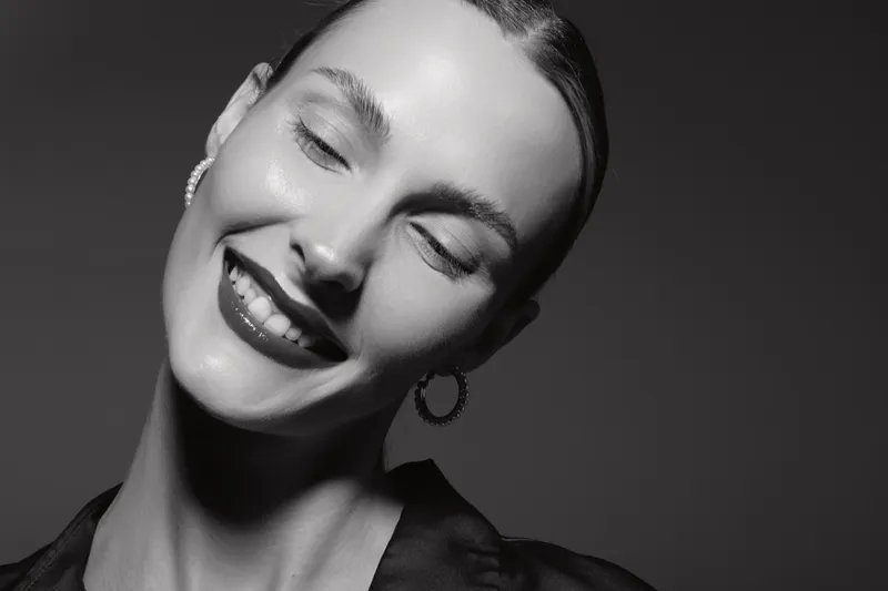 Closeup portrait of smiling caucasian woman with pale skin and earrings on black background studio. Beauty concept.