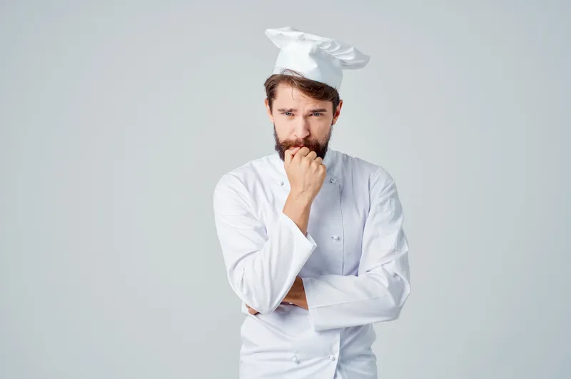 Бородатый мужчина-повар на кухне, жестикулирует руками на светлом фоне
