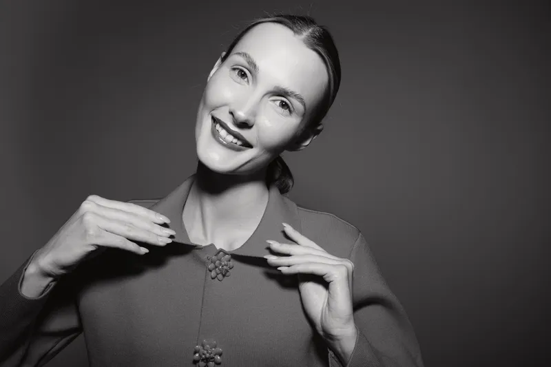 Smiling Caucasian woman with pale skin and hair tied back in a grey sweater posing confidently against dark background. Concept for happiness and portrait.