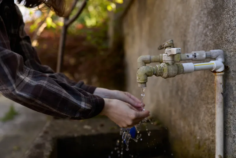 Hands under an outdoors faucet washing with water, a simple daily routine highlighting hygiene, cleanliness, and mindful self care in a casual natural setting