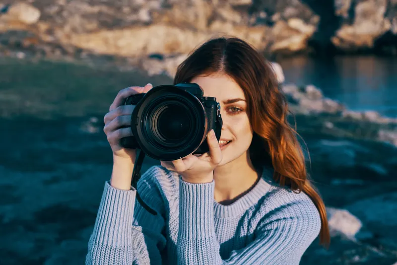 Рыжеволосая женщина-фотограф на фоне скалистых гор, профессиональная съемка на природе