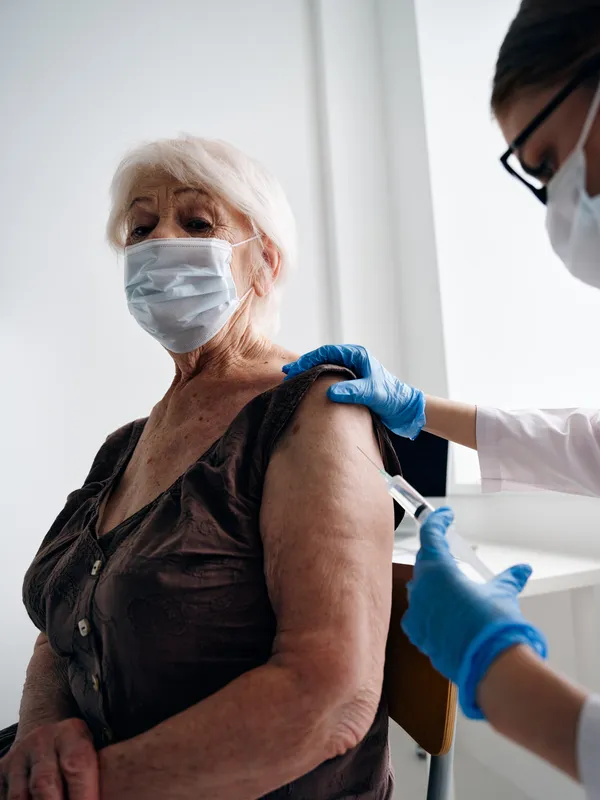 Врач делает инъекцию вакцины от COVID-19 женщине-пациентке, которая держит паспорт вакцинации