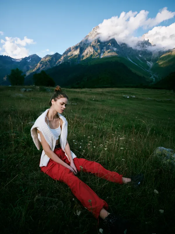 Woman sitting in a meadow with mountains in the distance, enjoying nature and fresh air, casual clothing, peaceful landscape, outdoor retreat, serene moment captured in scenic countryside
