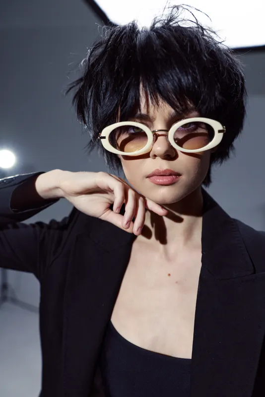 Stylish woman with short black hair wearing retro round sunglasses and dark outfit in a modern studio setting