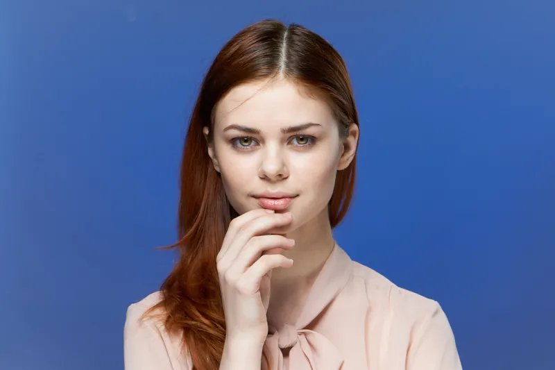 Симпатичная женщина в розовой рубашке, рука возле лица, на синем фоне