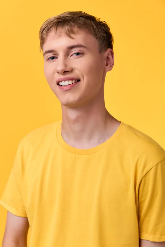 Smiling young man in a yellow t shirt stands against a yellow backdrop, conveying friendly mood, casual style and positive energy for lifestyle, fashion or advertising projects.
