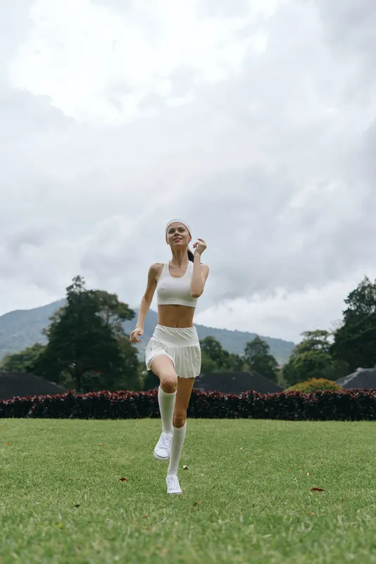 Young female athlete running joyfully in a sunny park, wearing a white sports outfit and enjoying the outdoor lifestyle, reflecting health and fitness