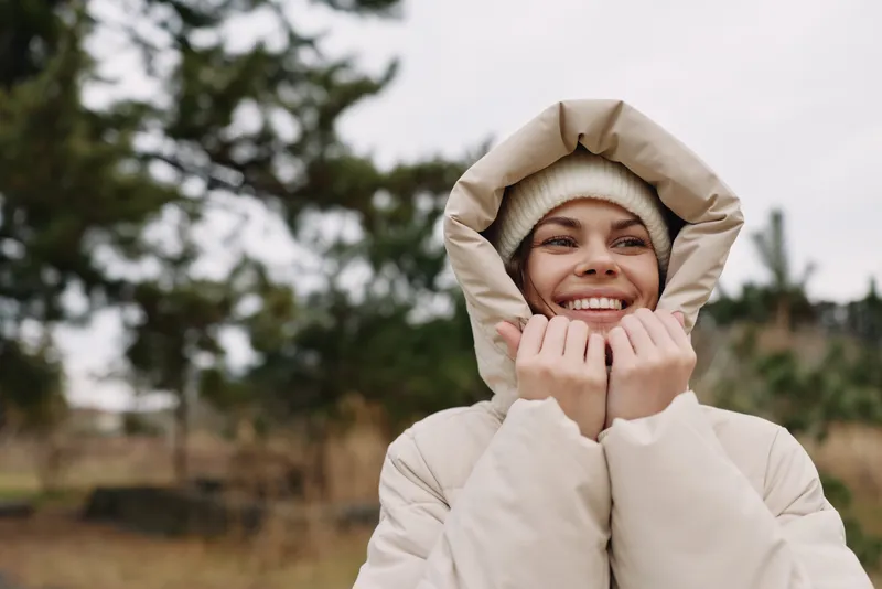 Winter outdoor portrait featuring a smiling woman in a padded coat with a hood, embracing chilly weather, soft lighting and cozy style for everyday fashion