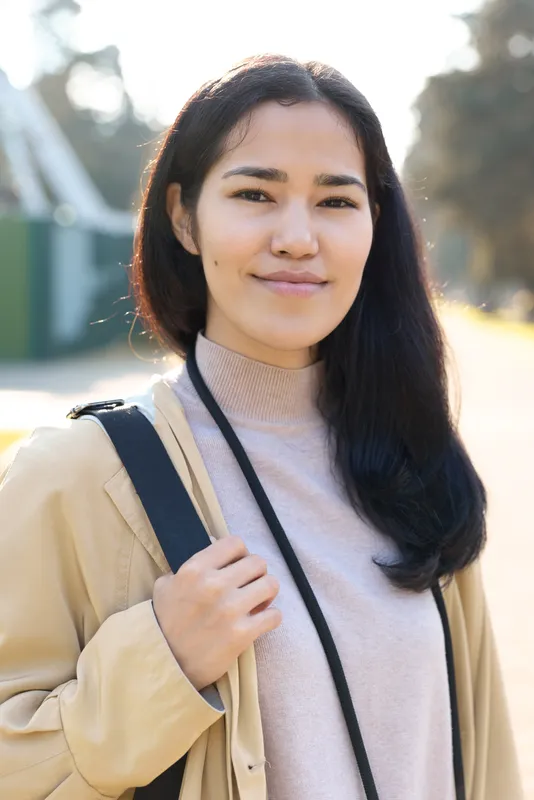 Woman outdoor casual professional backpack lanyard sweater beige jacket, smiling softly under warm daylight, showcasing versatile lifestyle style for education, travel, and work projects with natural