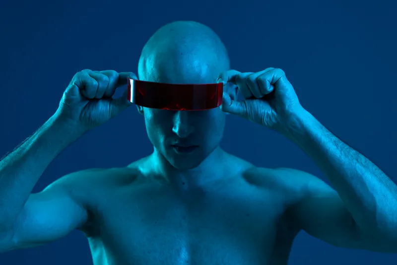 Futuristic man with red visor poses against a blue background, embracing a cyberpunk aesthetic. This captivating portrait showcases modernity and technology.