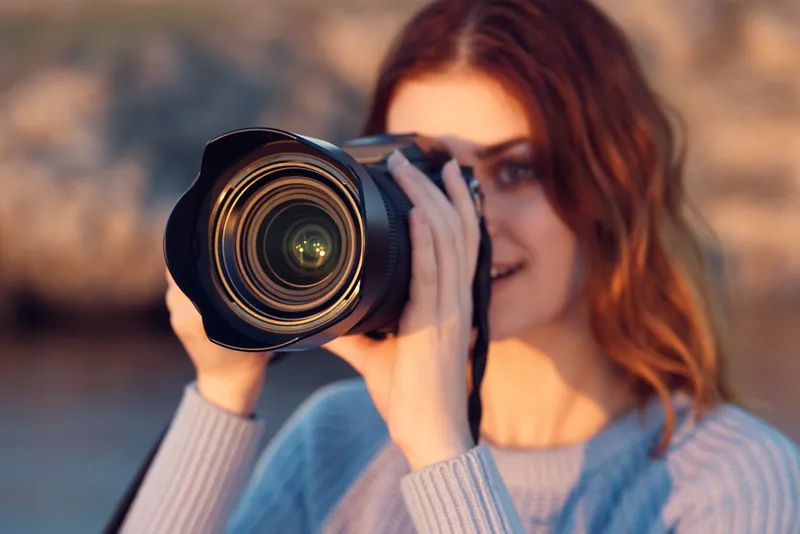 Женщина с фотоаппаратом в синем свитере в горах на открытом воздухе, обрезанный вид