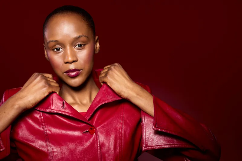 Confident African woman with dark skin wearing a red leather jacket on red background. Studio portrait with fashionable edgy style and strong direct gaze. Concept of beauty and empowerment.