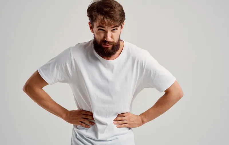 Мужчина прикасается рукой к животу, испытывая боль в области желудка