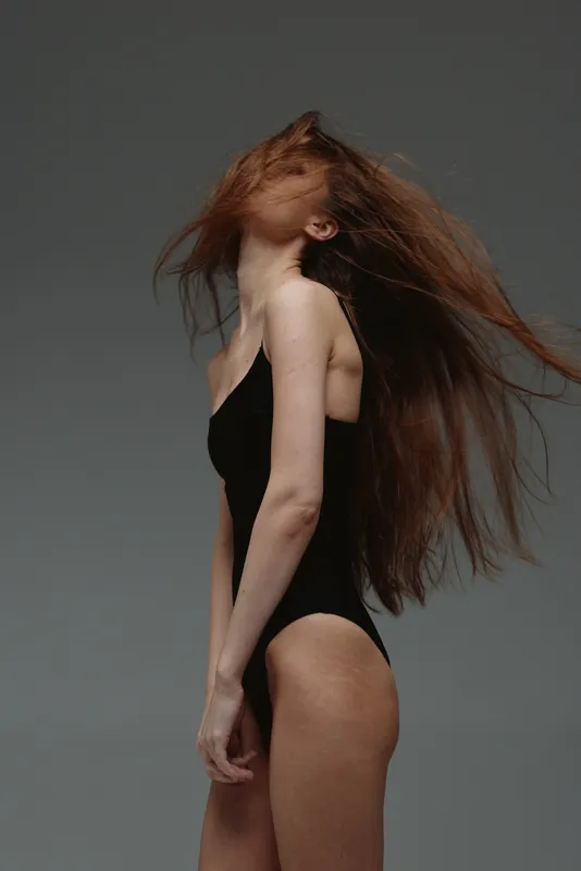 Woman with long hair in black outfit posing against grey background, elegant, dynamic, artistic, studio.