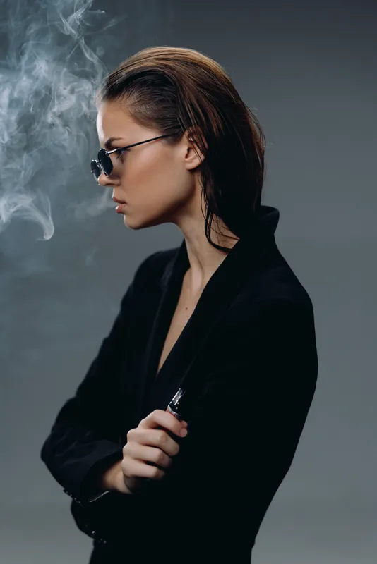 Profile of a stylish woman smoking vape with smoke against dark background
