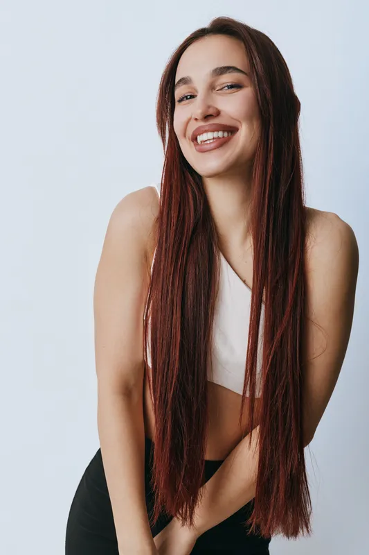Young woman with long braided hair smiling and posing in casual sportswear against plain background. Female model with confident expression and relaxed posture in studio.
