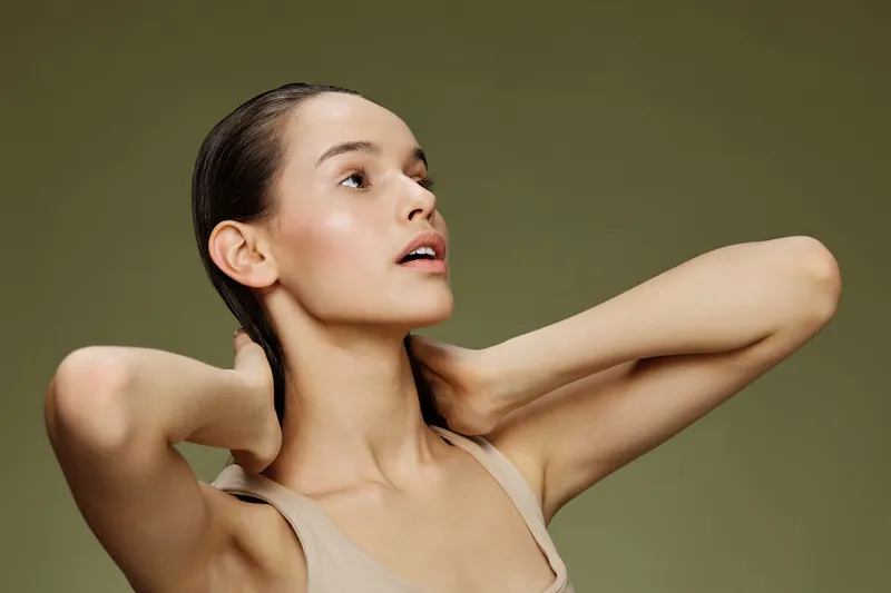 Elegant young woman with long hair styled, posing gracefully against a soft green background, expressing serenity and confidence in a minimalist look