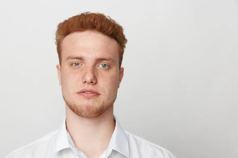 Portrait of a young redhead man with freckles and beard wearing a white shirt against a plain light background. Concept for natural beauty, youth, and casual style.