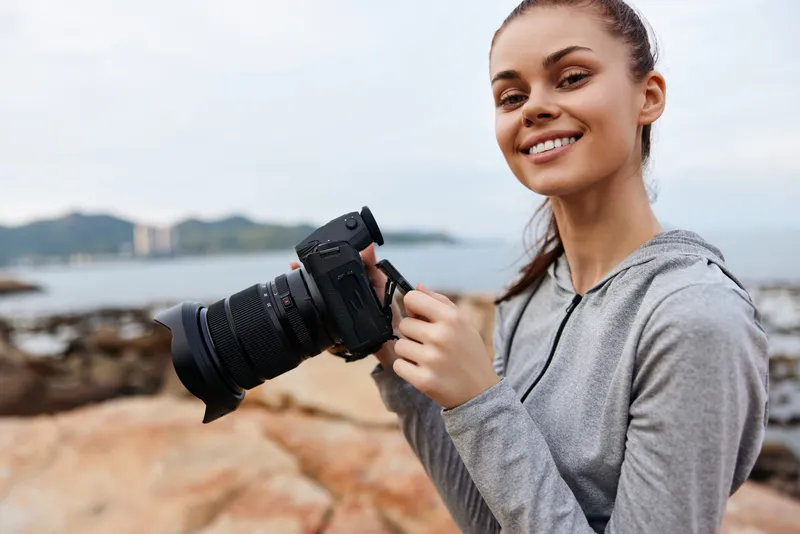 Young woman with a camera on the beach, smiling Casual sport clothing, coastal background, capturing memories, photography concept, outdoor lifestyle