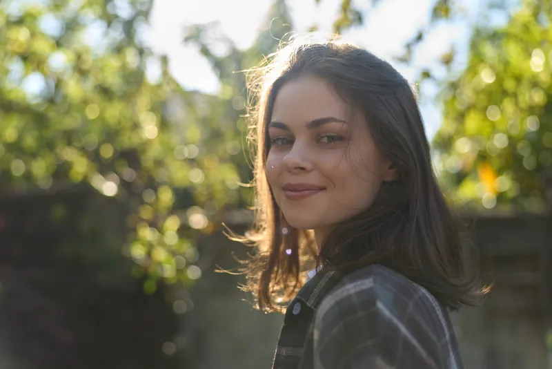 Portrait of a smiling woman in casual attire outdoors, bright natural light, relaxed lifestyle, candid moment in a lush garden setting